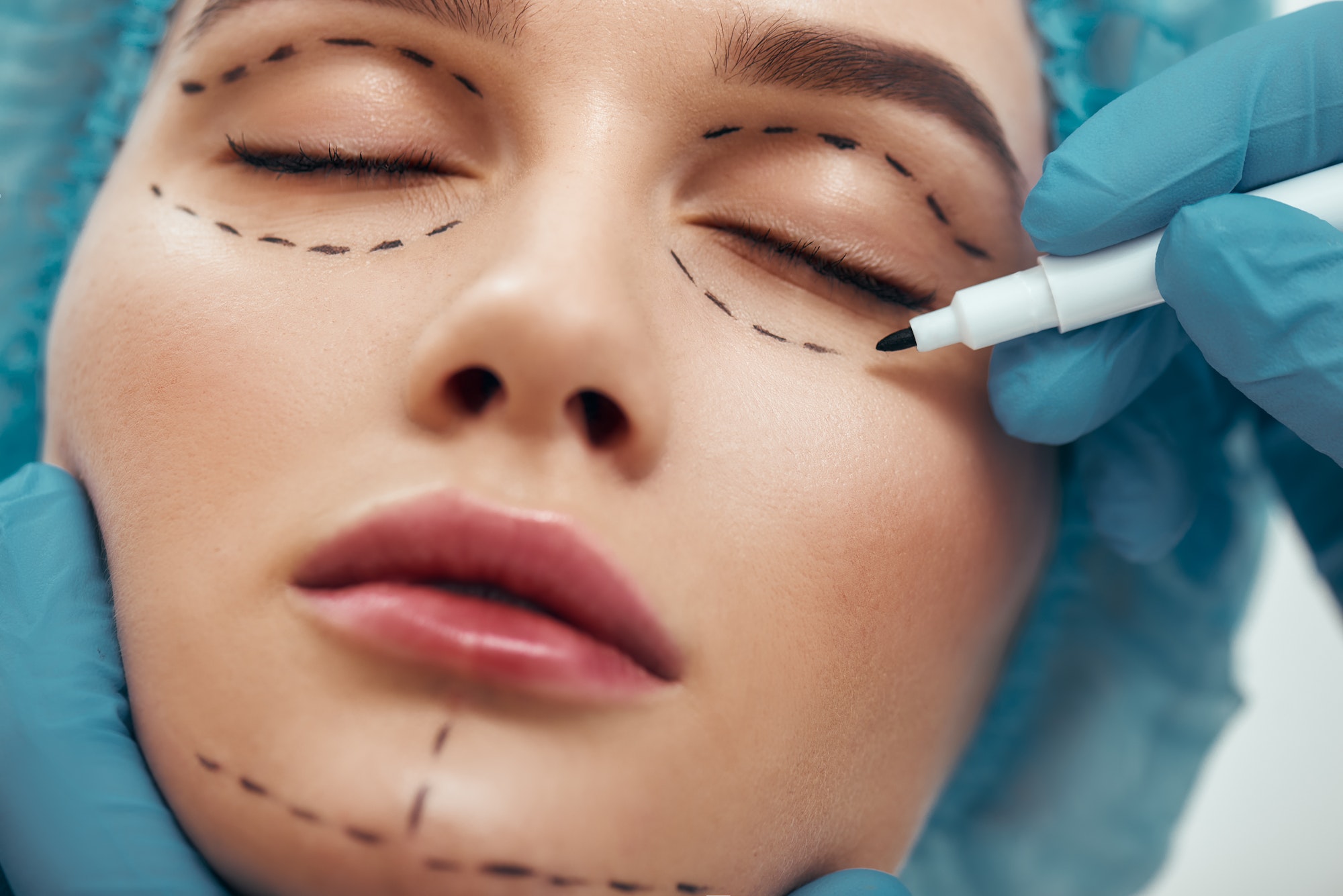 Close up photo of young woman with glowing skin in blue medical hat waiting for facial surgery